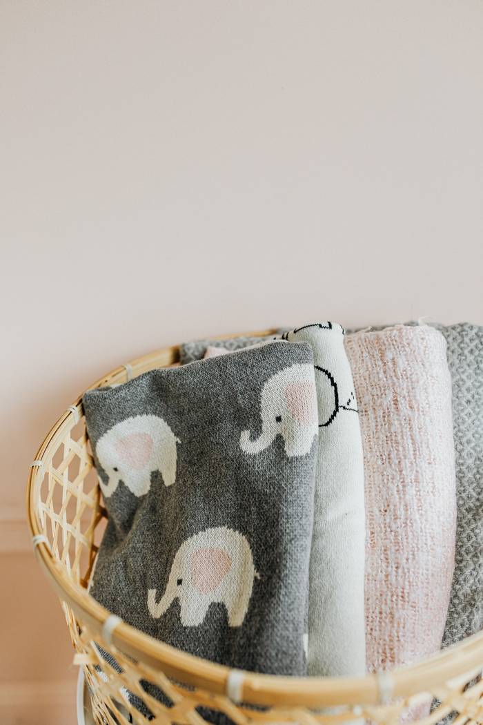 Folded baby blankets in a woven basket against a blush wall