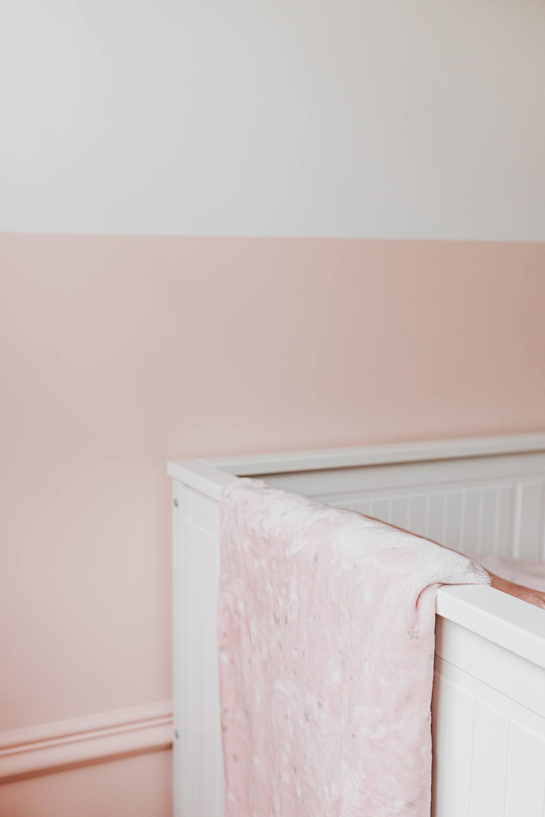 A calm nursery with soft pink walls and a white crib